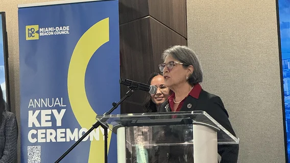 Woman with gray hair speaking at a podium microphone in front of an Annual Key Ceremony banner