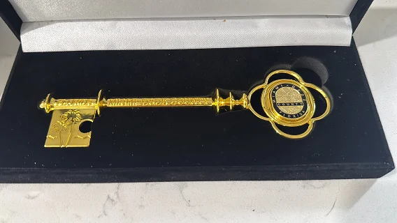 Gold ceremonial key with a decorative round emblem resting in a black velvet presentation case